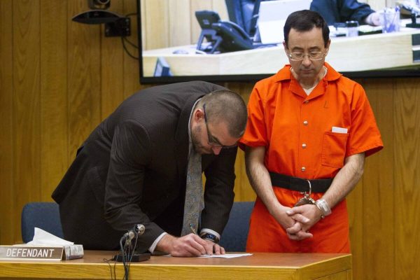 Defense attorney Matthew Newberg, left, signs court documents after Judge Janice Cunningham sentenced Larry Nassar, right, at Eaton County Circuit Court in Charlotte, Mich., Monday, Feb. 5, 2018. The former Michigan State University sports-medicine and USA Gymnastics doctor received 40 to 125 years for three first degree criminal sexual abuse charges related to assaults that occurred at Twistars, a gymnastics facility in Dimondale. Nassar has also been sentenced to 60 years in prison for three child pornography charges in federal court and between 40 to 175 years in Ingham County for seven counts of criminal sexual conduct. (Cory Morse /The Grand Rapids Press via AP)