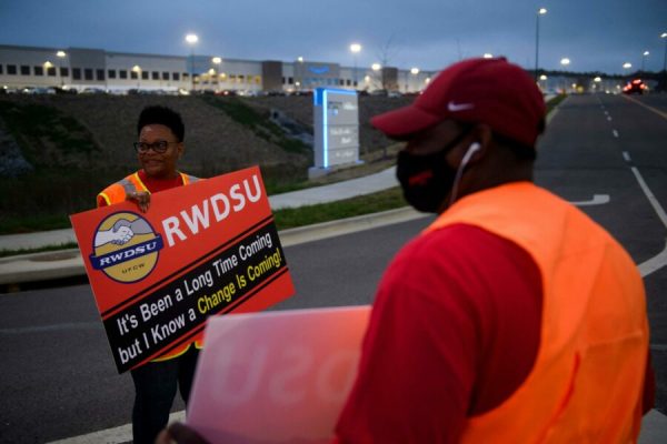 (FILES) In this file photo taken on March 27, 2021, Union organizers Syrena (L) and Steve (no last names given) wave to cars exiting an Amazon fulfillment center in Bessemer, Alabama. - A contentious unionization drive at an Amazon warehouse in Alabama failed as a vote count on April 9, 2021, showed a wide majority of workers rejecting the move. In a vote count seen online, National Labor Relations Board officials counted more than 1,608 "no" votes shortly before 1500 GMT, representing a majority of the 3,215 ballots cast. Slightly more than 600 votes favored the unionization effort organized by the Retail, Wholesale and Department Store Union. (Photo by Patrick T. FALLON / AFP)