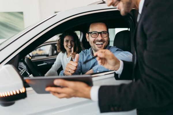 Middle age couple choosing and buying car at car showroom. Car salesman helps them to make right decision.