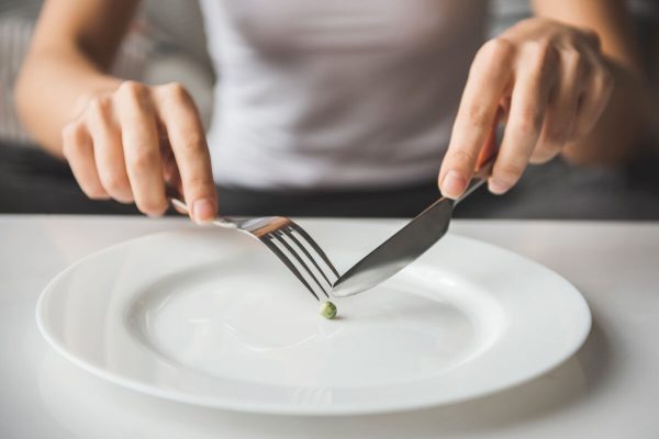 Suffering from anorexia. Cropped image of girl trying to put a pea on the fork