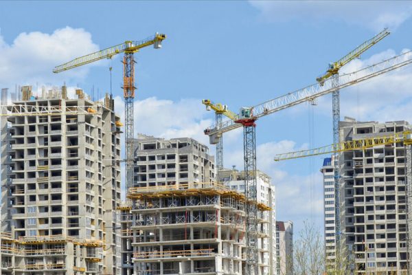 Construction site. Big industrial tower cranes with unfinished high raised buildings and blue sky in background. Scaffold. Modern civil engineering. Contemporary urban landscape.