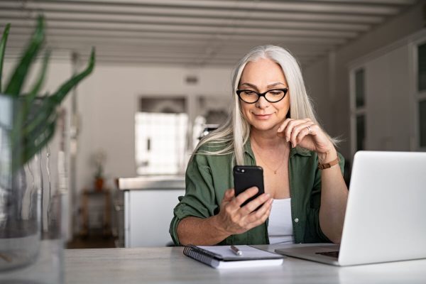 Happy,Senior,Woman,Using,Mobile,Phone,While,Working,At,Home