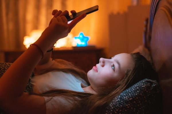 teen girls lying in bed at night and using smartphone. Insomnia and the harm of the smartphone before going to bed. Not healthy sleep. Dependence on social networks in adolescents.