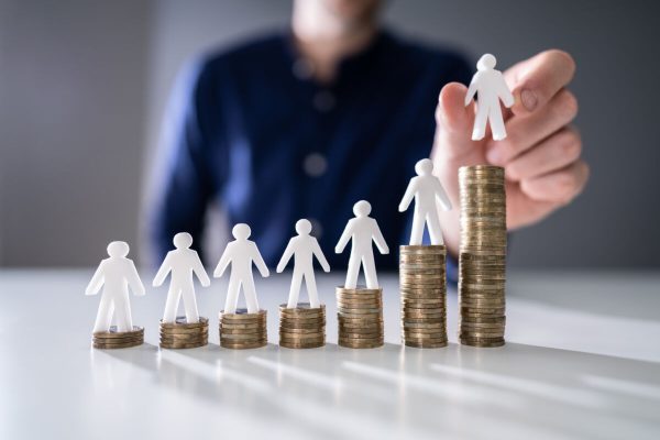 Human,Hand,Placing,Small,Human,Figure,On,Increasing,Stacked,Coins