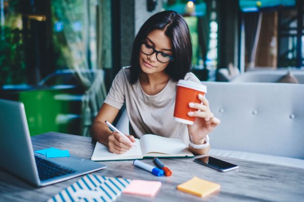 Concentrated,Female,Student,Writing,In,Notebook,While,Learning,With,Cardboard