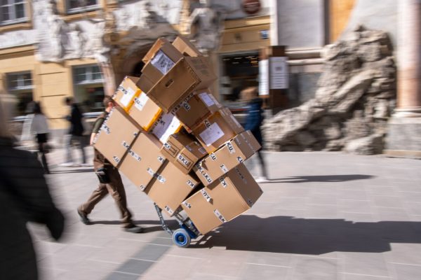 25 March 2021, Bavaria, Munich: A parcel delivery man transports several parcels with a hand truck through a pedestrian zone in the city centre. Photo: Peter Kneffel/dpa