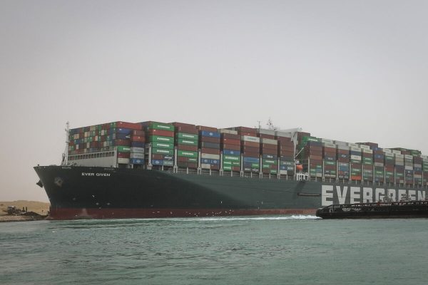 HANDOUT - 25 March 2021, Egypt, Suez: A tugboat sails past the "Ever Given", a container ship operated by the Evergreen Marine Corporation, which is currently stuck in the Suez Canal. The state-run Suez Canal Authority (SCA) announced on Thursday that navigation through the Suez Canal has been temporarily suspended until the full refloating of the Panamanian supertanker which ran aground on Tuesday in the southern end of the Suez Canal and blocked the traffic in both directions. The ship turned sideways in the Canal, while on route from China to Rotterdam, due to reduced visibility that resulted from a dust storm hitting the area, according to SCA. Photo: -/Suez Canal Authority/dpa - only for use in accordance with contractual agreement