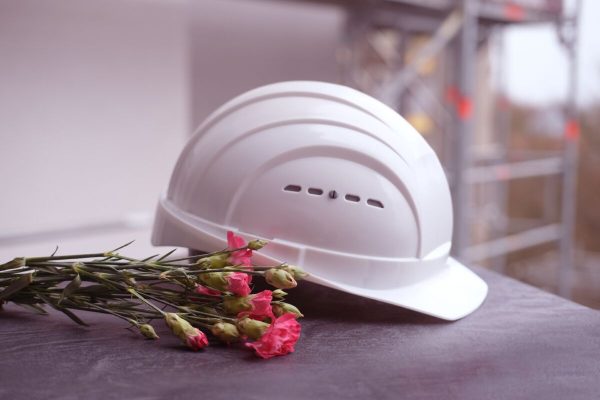 White,Hardhat,,Red,Carnations,,Helmet,On,Background,Of,Buildings,,Protection