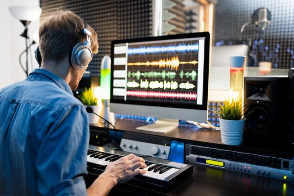 Young,Musician,With,Headphones,Pressing,Keys,Of,Piano,Keyboard,While