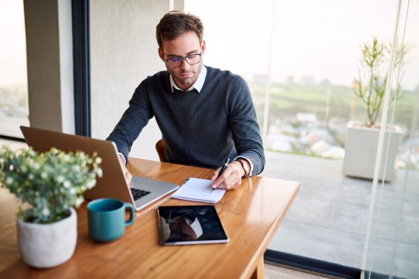 Young,Businessman,Sitting,At,A,Table,At,Home,Working,On