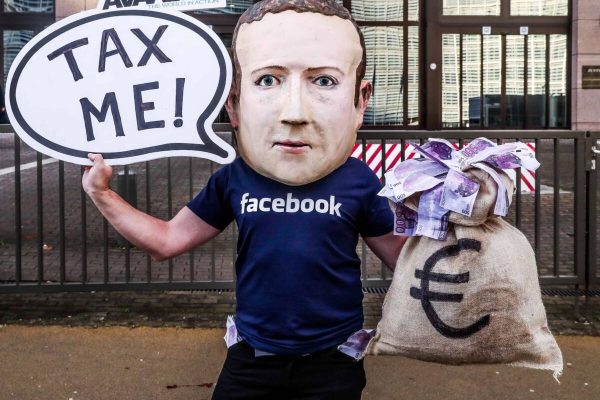 epa07207687 An activist wearing a mask depicting Facebook's CEO Mark Zuckerberg holds a banner reading 'Tax me' at the start of an European Union Finance Ministers Meeting in front of the European Council in Brussels, Belgium, 04 December 2018. Activists ask for an EU tax on big digital firms.  EPA/STEPHANIE LECOCQ